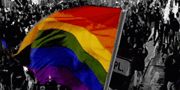 An animated rainbow flag waving above a marching crowd. 
