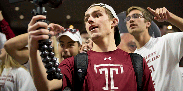Moving photo of Brandon Kane filming himself with Temple fans behind him.