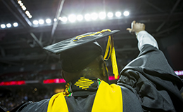 A male student pointing up while wearing his cap and gown.