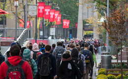 Students walking on campus underneath red flags bearing the Temple ‘T’.