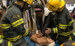 Two firefighters teaching a female student how to perform CPR.