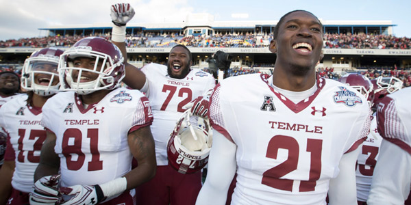 Temple football players smiling and celebrating on the field after a big win. 
