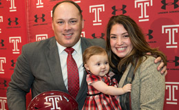 Geoff Collins holding a Temple helmet and smiling with wife and baby daughter.