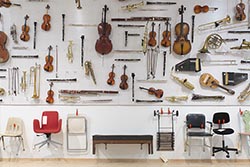 A large display of musical instruments and chairs hanging on a gallery wall.