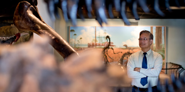 Roger Ideishi standing among dinosaur bones in a museum