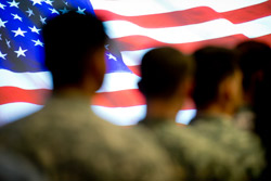 People in Army fatigues standing with American flag in background 