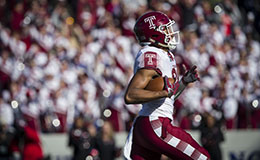 A Temple football player holding the ball and running with fans in the background.  