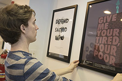 A student hanging a poster with text that reads 'give me your tired, your poor'.