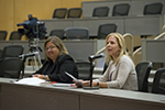 Two women sitting at a table and one is speaking into a microphone.