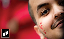A close up of a man with a red Temple “T” painted on his face.