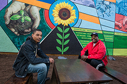 Two men sitting in front of a new colorful mural in North Philadelphia