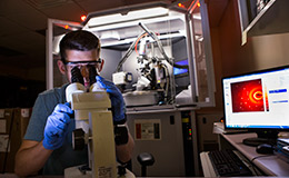 A male researcher looking through a microscope in a lab.