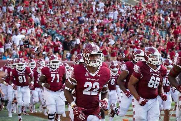 Temple players take the field in front of stands filled with Cherry and White.